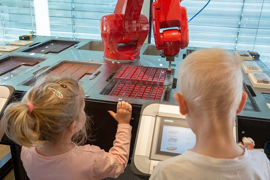 Otroka opazujeta čokoladnega robota med izdelavo čokoladnih tablic v čokoladnici Zotter.