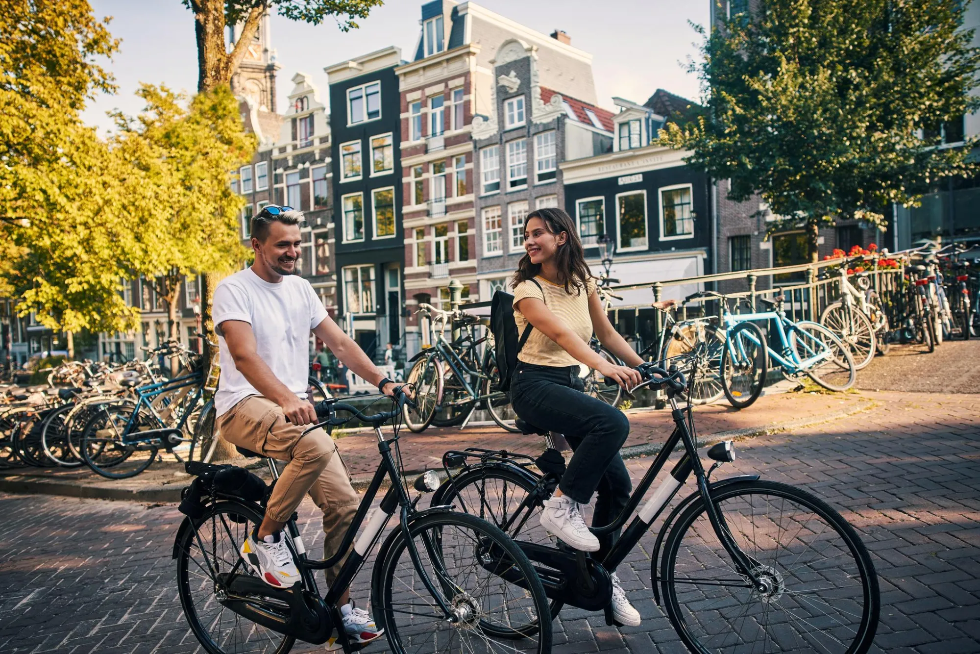 Par raziskuje Amsterdam s kolesom med kanali in značilnimi ozkimi hišami v središču mesta.