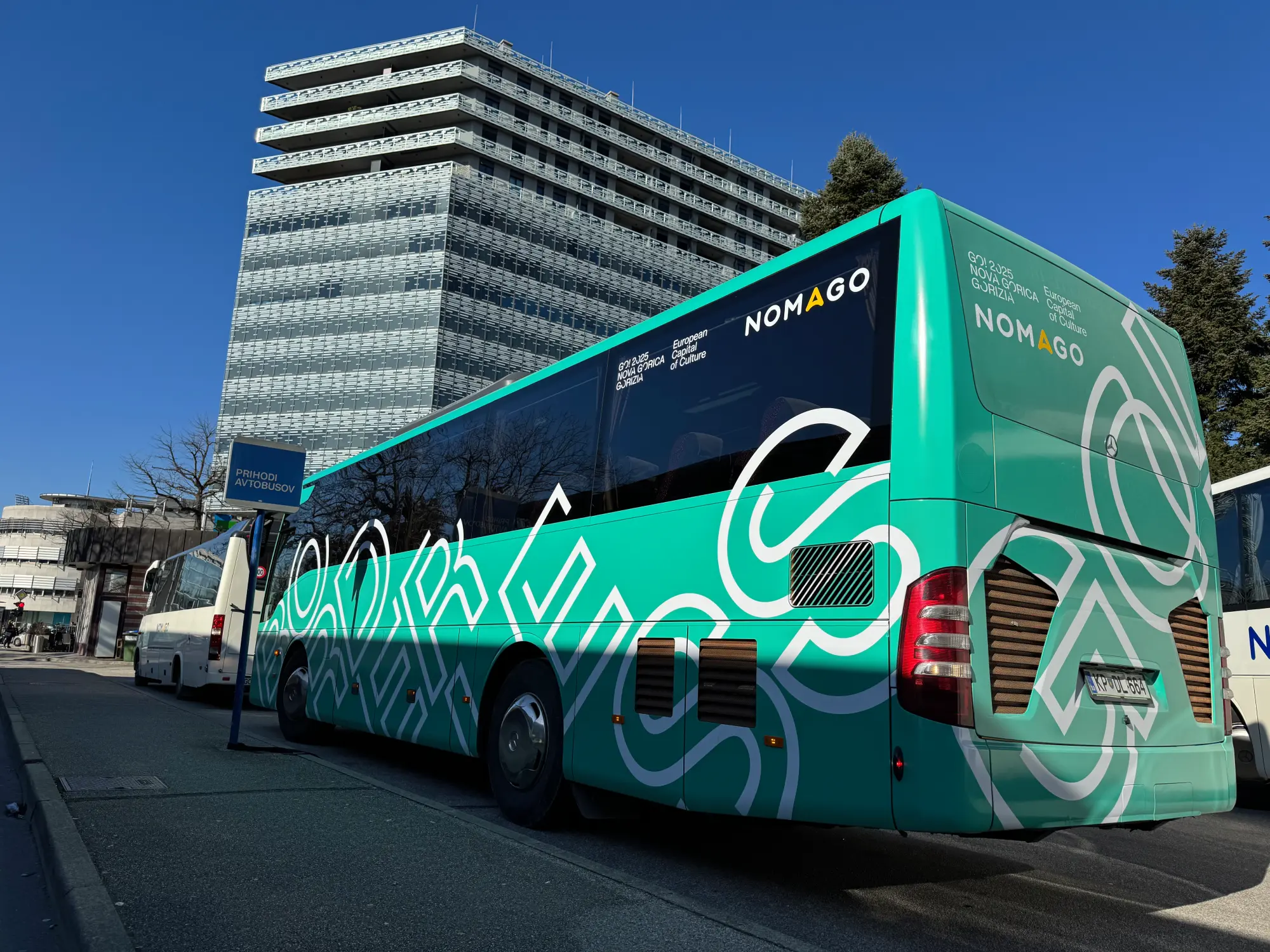 Zelen Nomago avtobus slikan od vzadaj pred visoko stavbo na avtobusnem postajališču