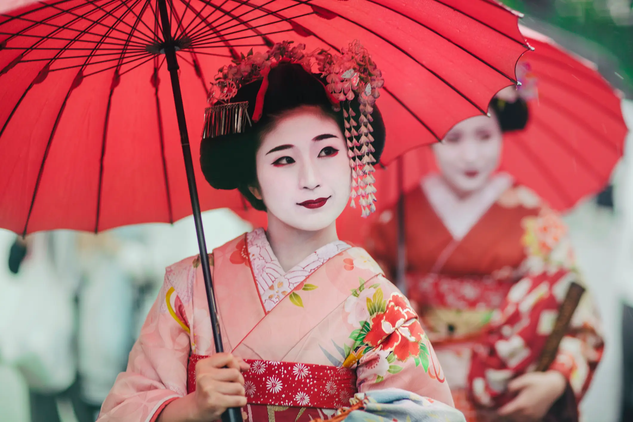 Japonska umetnica v tradicionalnem kimonu z rdečim senčnikom.