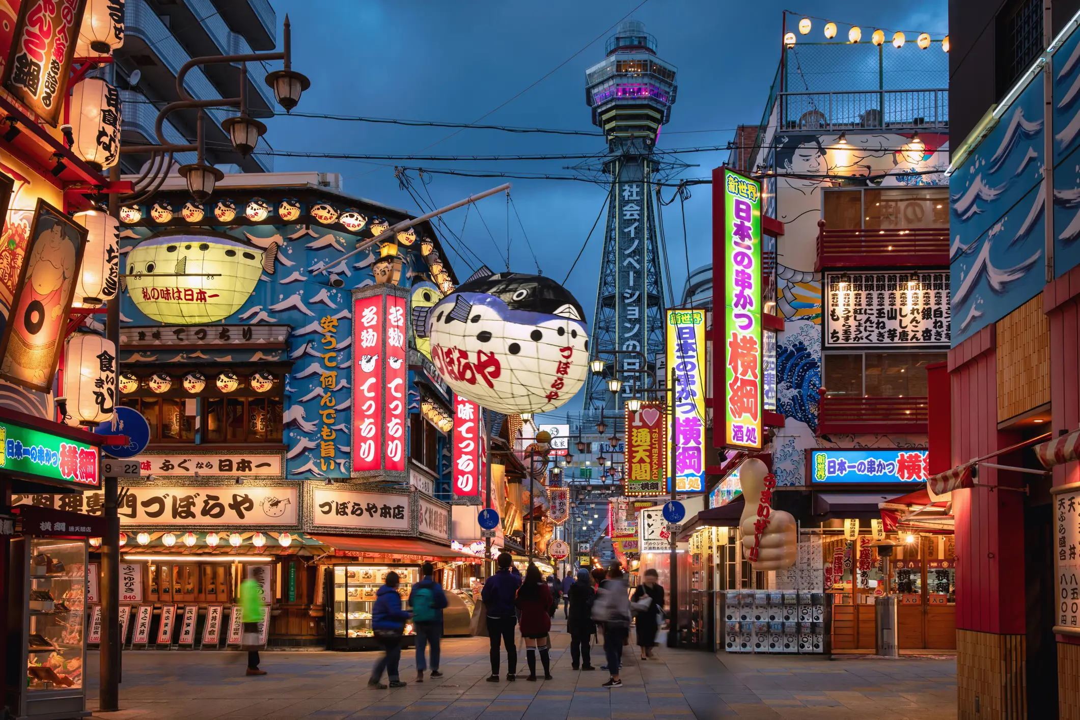 Večerni utrip četrti Shinsekai v Osaki z ljudmi na ulici in stolpom Tsutenkaku v ozadju