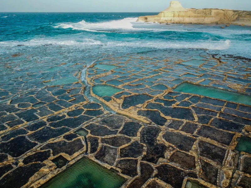 Pogled iz zraka na otok Gozo z obalnimi solinami in turkiznim morjem.