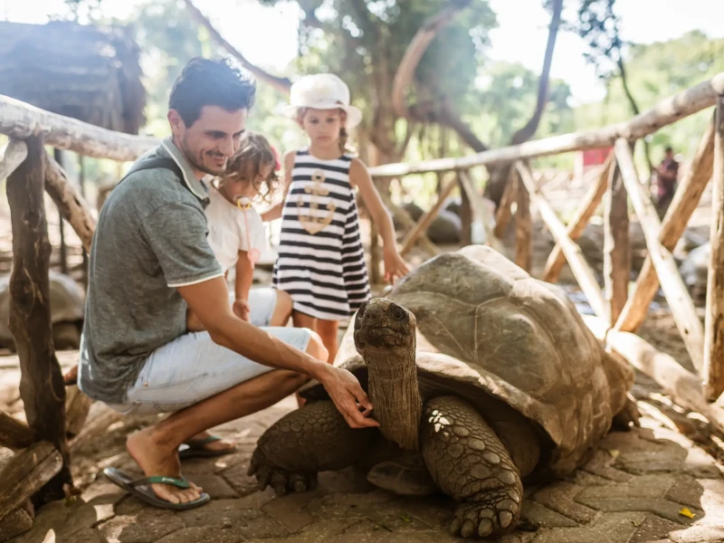 Družina si ogleduje velikansko želvo na otoku Prison Island pri Zanzibaru.