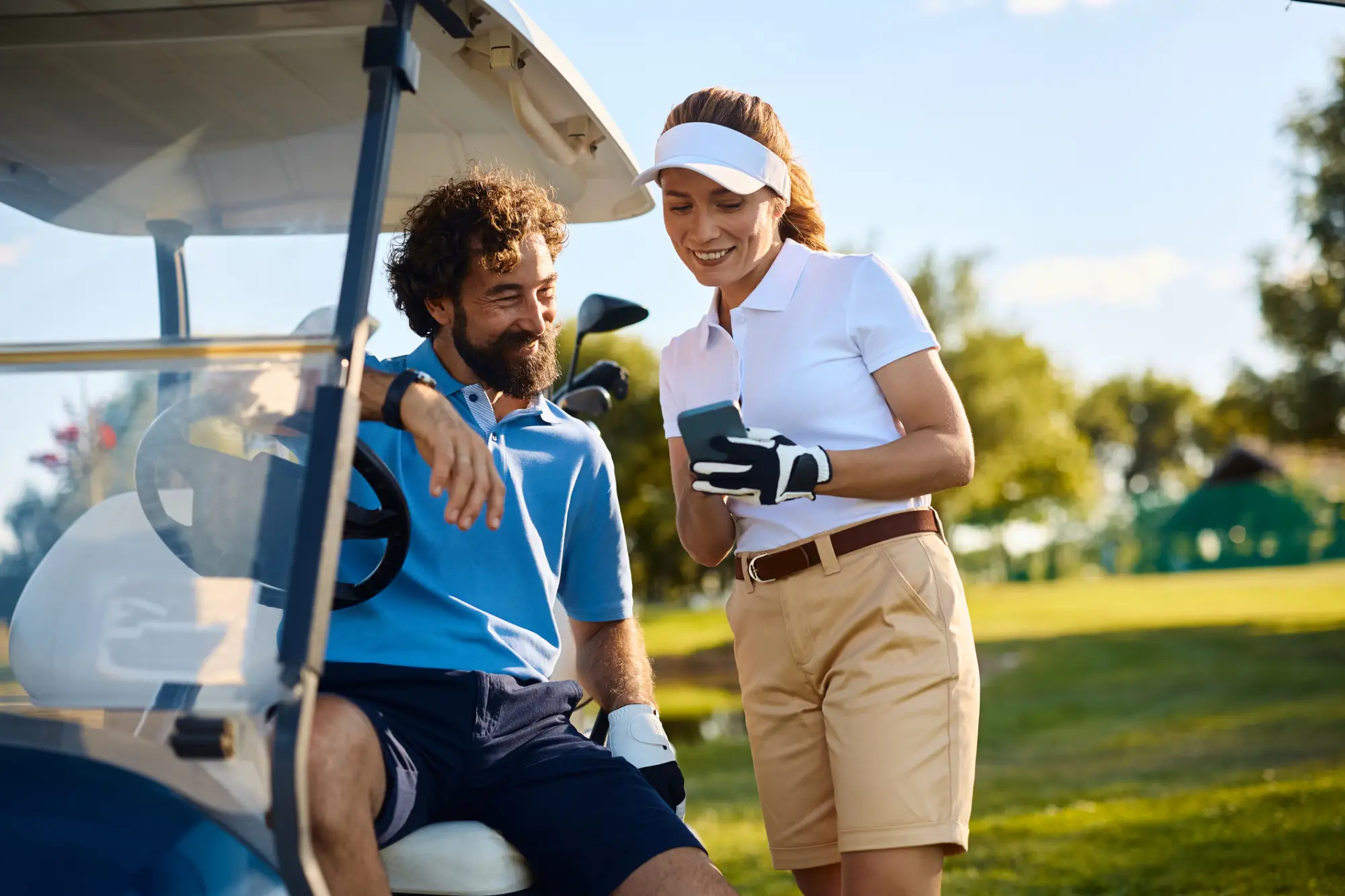 Par na golf kartu gleda na telefon