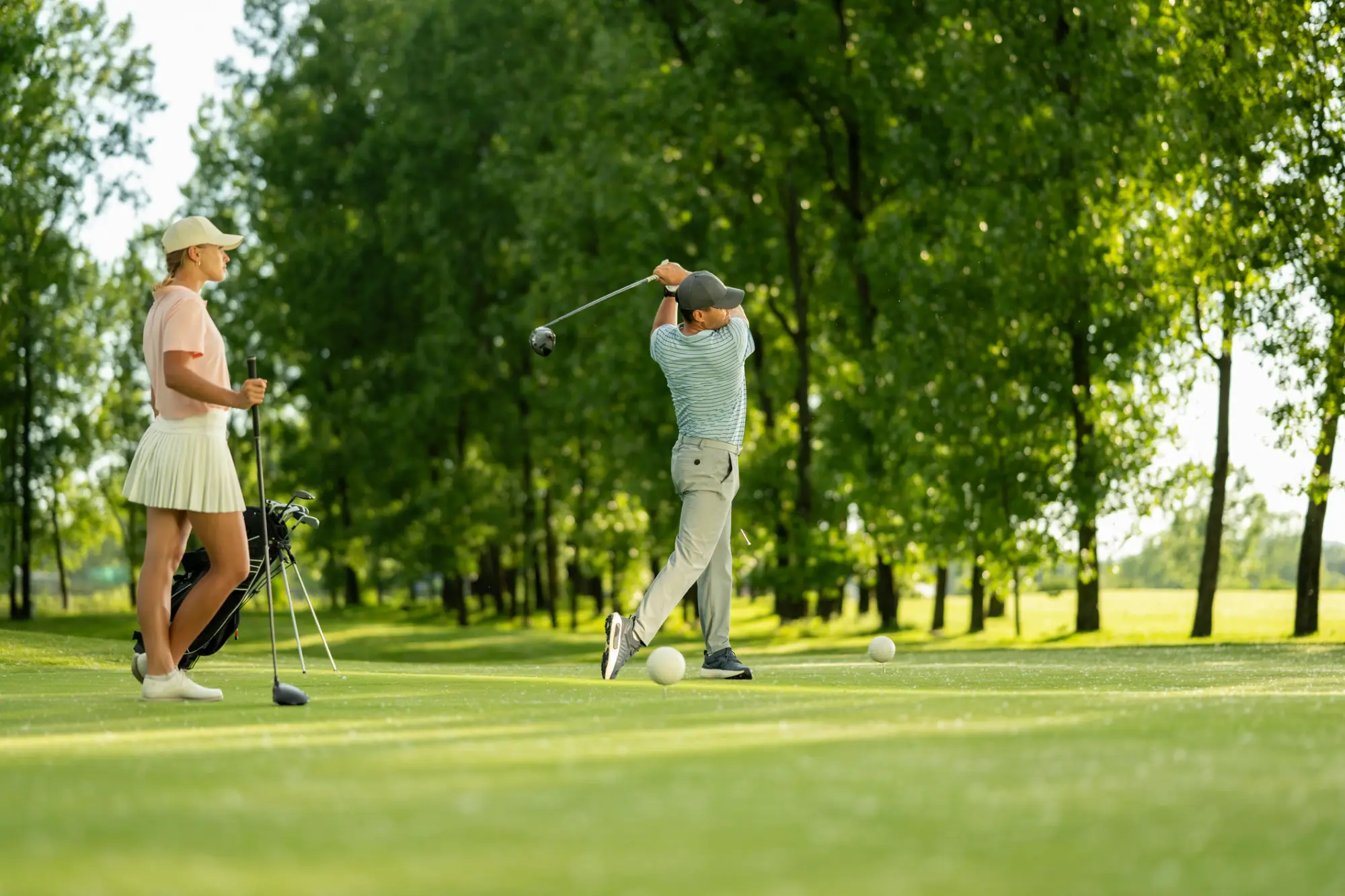 Golfistka gleda golfista kako udarja žogico