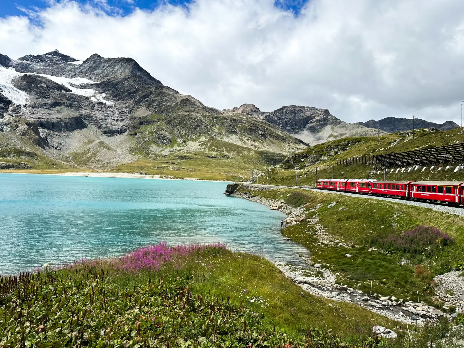 Vlak Bernina Express vozi ob turkiznem jezeru Lago Bianco med švicarskimi Alpami.